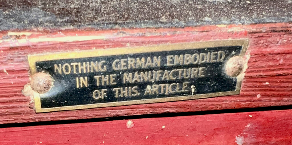 Bench placard embossed on a red bench in gold text against a black background. The text reads "Nothing German embodied in the manufacture of this article:.