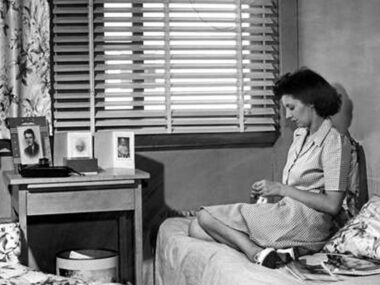 Black and white photograph of a woman sitting on a bed from the WWII era.